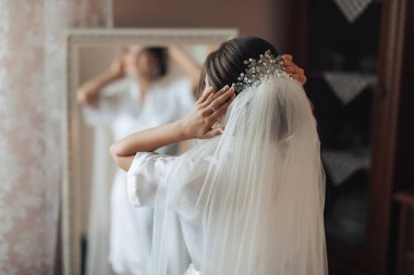 Bir kadın düğünü için hazırlanıyor ve duvağını takıyor. O bir aynanın önünde duruyor.