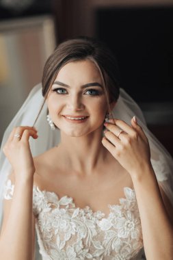 Bir kadın düğünü için hazırlanıyor ve duvağını takıyor. Gülümsüyor ve kameraya bakıyor.