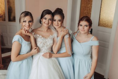 Bir gelin ve nedimeleri resim için poz veriyor. Gelin beyaz bir elbise giyiyor ve nedimeler mavi elbiseler giyiyor. Sahne mutlu ve kutlama dolu, gelin olarak.