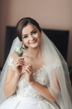 Bir gelin beyaz bir gelinlik giyerken elinde bir çiçek tutuyor. Gelin düğün gününde fotoğraf çektirmek için poz verirken mutluluk ve kutlama kavramı.