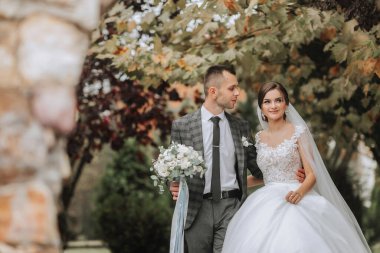 Bir gelin ve damat bir buket ve kravatla yolda yürüyorlar. Gelin beyaz bir elbise giyiyor ve damat bir takım elbise giyiyor. Sahne mutlu ve kutlama dolu, çünkü çift evleniyor.