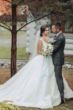 Gelin ve damat bir ağacın önünde, gelin bir buket tutuyor.