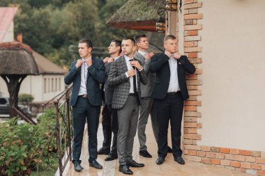 Takım elbiseli bir grup adam binanın dışında bekliyor. Hepsi resmi giyinmiş ve bir şeye bakıyorlar.