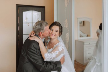 Bir adam bir kadının yanağını öpüyor. Kadın gelinlik giyiyor.