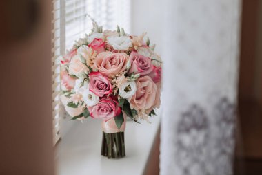 Bir buket pembe çiçek pencere pervazında duruyor. Çiçekler bir vazoda düzenlenir ve çeşitli boyutlardadır. Buket, doğanın dokunuşunu ekleyen güzel ve renkli bir görüntüdür.