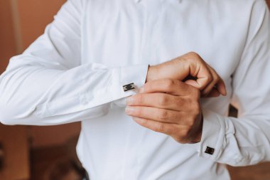 Bir adam beyaz gömlek giymeye hazırlanıyor ve kelepçesini ayarlıyor. Formalite ve detaylara dikkat etme kavramı. Çünkü adam uygun bir şekilde giyinmeye zaman ayırıyor.