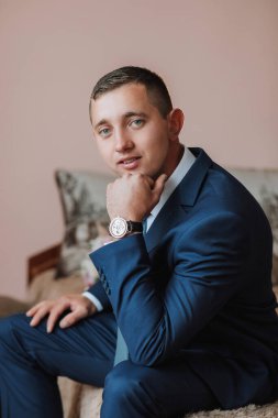 Takım elbiseli ve kravatlı bir adam kanepeye oturur ve kameraya bakar. O bir saat takıyor ve dalgın bir ruh hali içinde.