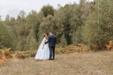 Bir gelin ve damat düğün günlerinde ormanda yürüyorlar. Gelin beyaz bir elbise giyiyor ve damat mavi bir takım elbise giyiyor. Sahne romantik ve huzurlu.