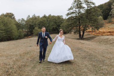 Bir gelin ve damat düğün günlerinde bir tarlada yürüyorlar. Gelin beyaz bir elbise giyiyor ve damat mavi bir takım elbise giyiyor. Sahne mutlu ve kutlama dolu.