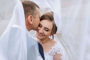 Bir gelin ve damat beyaz bir peçenin altında öpüşüyor.