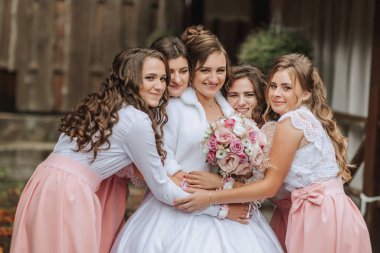 Bir gelin ve nedimeleri resim için poz veriyorlar. Gelin beyaz bir elbise giyiyor ve nedimeler pembe elbiseler giyiyor. Gelin elinde bir buket çiçek tutuyor.