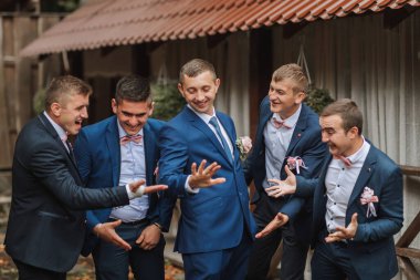 Takım elbiseli bir grup adam fotoğraf için poz veriyor. Adamlardan biri kravat takmış ve pembe fiyonk takmış.