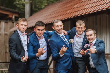 Takım elbiseli ve kravatlı beş adamdan oluşan bir grup fotoğraf için poz veriyor. Hepsi gülümsüyor ve elleri kalçalarında. Sahne neşeli ve eğlenceli, çünkü erkekler birlikte poz veriyorlar.