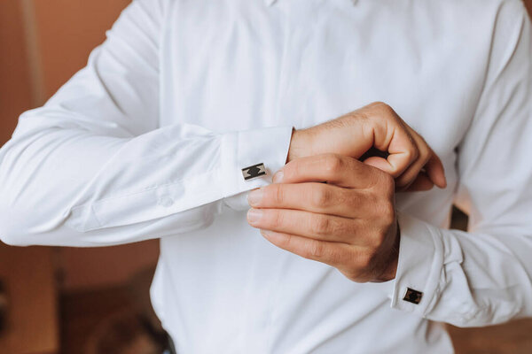 A man is getting ready to dress up in a white shirt and is adjusting his cuff. Concept of formality and attention to detail, as the man takes the time to properly dress himself
