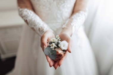 Bir kadın elinde bir buket çiçek tutuyor. Çiçekler beyaz ve yeşildir ve onları çiçek açmış gibi gösterecek şekilde düzenlenmişlerdir.