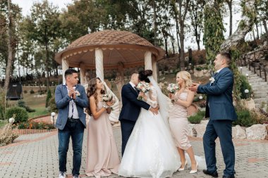 Bir grup insan, ortasında bir gelin ve damat olan bir resim için poz veriyor. Gelin beyaz bir elbise giyiyor ve damat da takım elbise giyiyor.