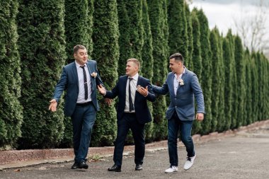 Takım elbiseli üç adam sokakta yürüyor, biri diğer ikisiyle el ele tutuşuyor.