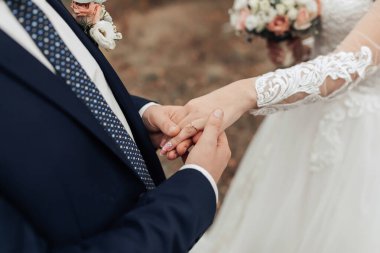 Bir erkek ve bir kadın evleniyor ve alyanslarını takmak üzereler. Gelin beyaz bir elbise giyiyor ve damat mavi bir takım elbise giyiyor. Gelinin saçında bir çiçek var.