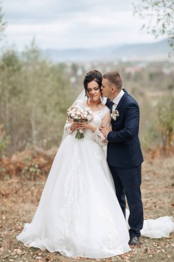 Bir gelin ve damat tarlada öpüşüyor. Gelin elinde bir buket çiçek tutuyor.