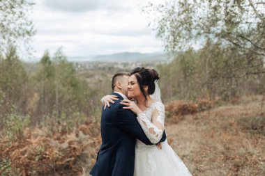 Bir gelin ve damat ormanda birbirlerine sarılırlar. Gelin beyaz bir elbise giyiyor ve damat mavi bir takım elbise giyiyor. Sahne sıcak ve sevgi dolu.