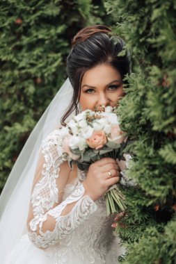 Bir gelin elinde bir buket çiçek tutarken çalıların arkasında saklanıyor. Mahremiyet ve mahremiyet kavramı, gelinin yeşillik tarafından kısmen gizlenmesi gibi.