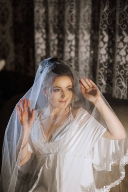 Bir kadın peçe takıyor ve kameraya bakıyor. Beyaz bir elbise ve beyaz bir duvak giyiyor.