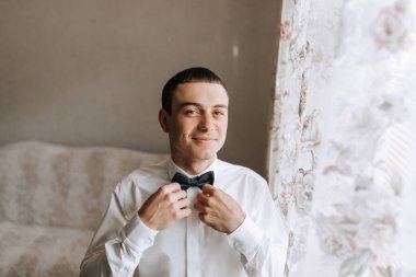 Bir adam papyon takmaya hazırlanıyor. Gülümsüyor ve kameraya bakıyor.