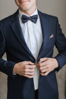 Takım elbiseli ve kravatlı bir adam mavi ceket ve beyaz gömlek giyiyor. Kravatını düzeltiyor ve ellerini cebinde tutuyor. Formalite ve profesyonellik kavramı