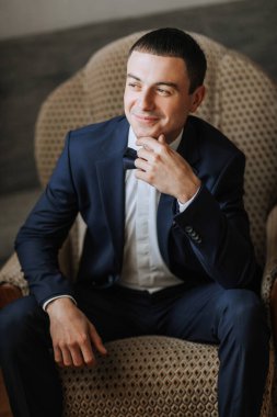 Takım elbiseli ve papyonlu bir adam sandalyede oturur. Gülümsüyor ve mutlu.