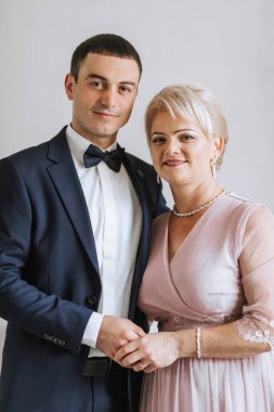 Bir adam ve bir kadın resim için poz veriyorlar. Kadın pembe bir elbise giyerken adam takım elbise ve kravat takıyor. İkisi de gülümsüyor ve anın tadını çıkarıyor gibi görünüyorlar.