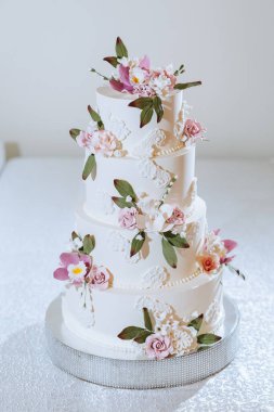 Dört katlı bir düğün pastası, pembe çiçekler ve beyaz kremalı.