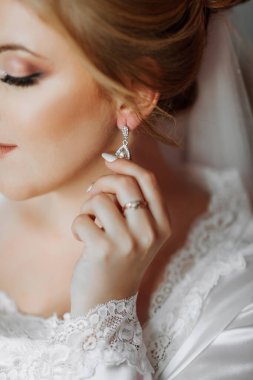 Bir kadın bir çift küpe ve yüzük takıyor. Beyaz bir elbise giyiyor ve eli kulağında.