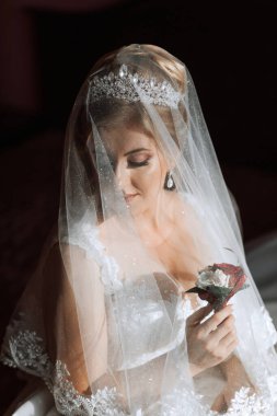 Duvak takan ve elinde çiçek tutan bir kadın. Peçe dantelden yapılmıştır ve çiçek kırmızıdır.