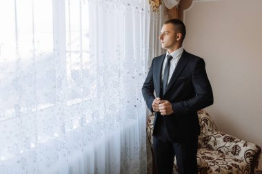 Takım elbiseli bir adam pencerenin önünde duruyor, sokağa bakıyor. O bir kravat takıyor ve bir etkinlik için hazırlanıyor. Formalite ve beklenti kavramı