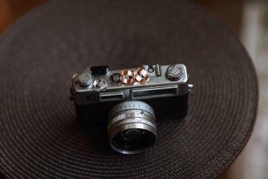 Üzerinde yüzük olan bir kamera siyah ve kahverengi bir yüzeye oturur. Kamera eski ve ona klasik bir görünümü var. Sahne nostaljik bir hava veriyor.