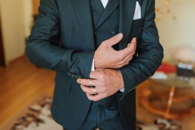 Takım elbiseli bir adam kelepçesini ayarlıyor. Takım elbise siyah ve adam beyaz gömlek giyiyor.