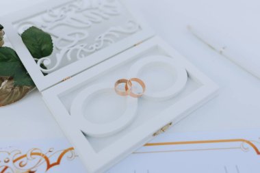 İçinde iki yüzük olan beyaz bir kutu. Yüzükler altındır ve beyaz bir arkaplanın üzerine yerleştirilir.