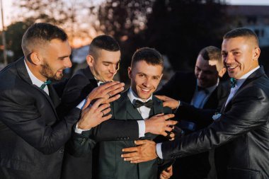 Takım elbiseli bir grup adam birbirlerine sarılıyorlar. Sahne mutlu ve dostane.
