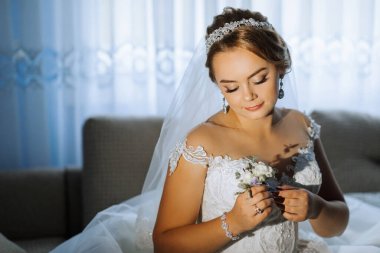 Bir gelin düğünü için hazırlanıyor ve duvağını takıyor. Elinde bir çiçek tutuyor.