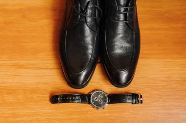 Bir çift siyah ayakkabı ve bir saat ahşap bir yüzey üzerinde sergilenir. Ayakkabılar ve saat hem klasik hem de zamansız olduğu için zarafet ve sofistike anlayışı.