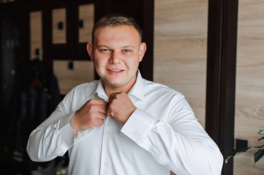 Beyaz gömlekli bir adam duvarın önünde duruyor ve gömleğini düzeltiyor. Formalite ve detaylara dikkat etme kavramı. Çünkü adam gömleğini düzgün bir şekilde içeri sokuyor.