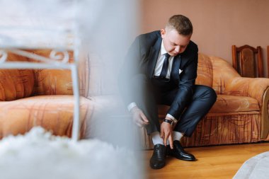 Takım elbiseli bir adam kanepede oturuyor, ayakkabılarını tamir ediyor. Adamın resmi bir ortamda olmadığı için, resmin rahat ve rahat bir havası var.