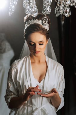 Beyaz cüppeli bir kadın elinde küçük bir nesne tutuyor. Kadın bir taç ve peçe takıyor.