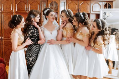 Bir grup kadın bir fotoğraf için poz veriyor, içlerinden biri gelinlik giyiyor. Sahne neşeli ve kutlayıcı, çünkü kadınlar büyük ihtimalle bir düğüne ya da diğer özel etkinliklere katılıyorlar.