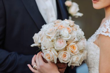 Bir gelin ve damat bir buket beyaz çiçek tutuyorlar. Gelin beyaz bir elbise giyiyor ve damat bir takım elbise giyiyor. Çiçekler bir vazoda sergileniyor ve çift resim için poz veriyor.