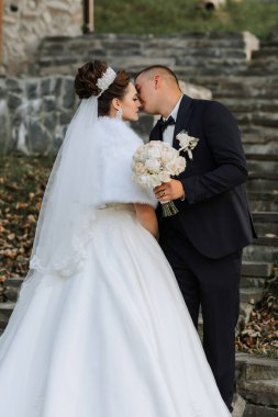 Bir gelin ve damat merdivenlerde öpüşüyor. Gelin beyaz bir elbise ve duvak takıyor. Bir buket çiçek ve çiçek tutuyorlar.