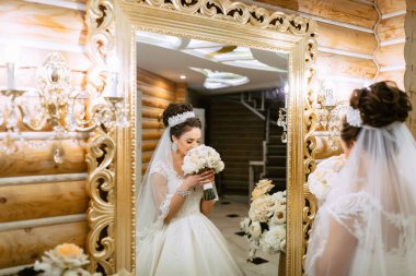 Bir gelin elinde bir buket çiçekle aynaya bakıyor. Ayna, gelinin güzelliğini ve zarafetini yansıtan gösterişli ve altındır. Romantizm ve kutlama kavramı