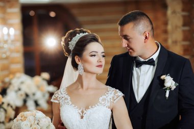 Bir gelin ve damat kilisede birlikte duruyorlar. Gelin beyaz bir elbise ve duvak takarken damat siyah bir takım elbise ve papyon takıyor. Sahne muhtemelen bir düğün merasimi.