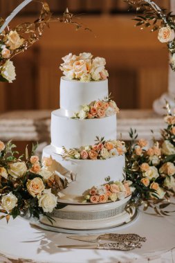Üzerinde çiçekler olan üç katlı bir düğün pastası. Pasta beyaz ve gümüş bir tabanı var.