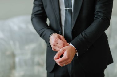 Takım elbiseli bir adam kravatını takmaya hazırlanıyor. Sol bileğinde gümüş bir bilezik var.